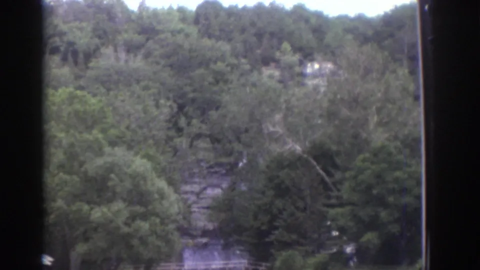 The Watkins Glen travel footage ends on a wooded ravine scene with rock ledges and a small waterfall or stream among trees.