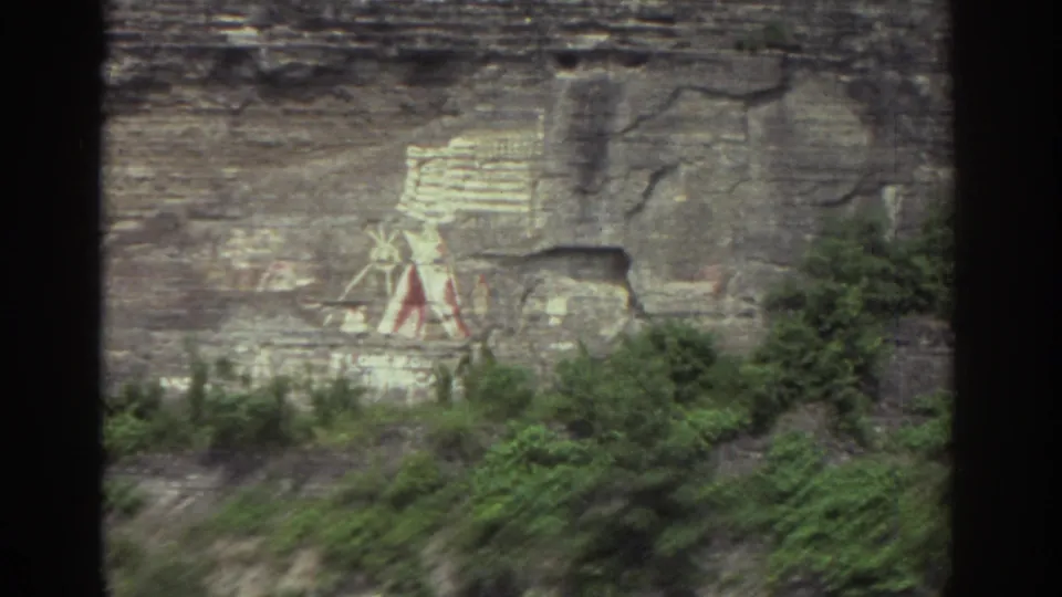 1976 Watkins Glen river-tour view of the cliff mural through a boat window, with layered stone, brush, and dark window framing.