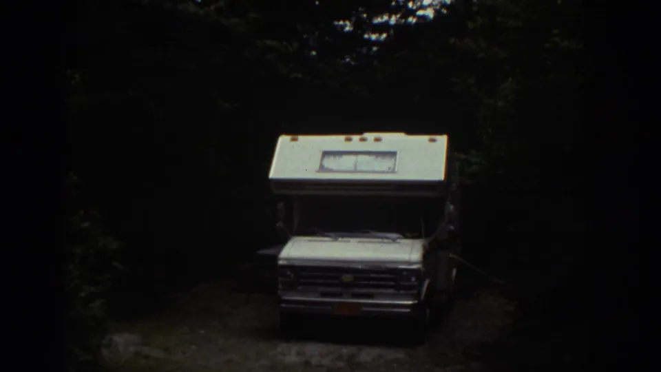1976 Watkins Glen travel footage shows a white vintage RV parked among trees in a shaded wooded area.