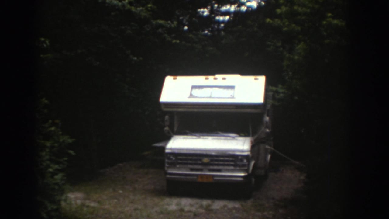 1976 Watkins Glen home-movie frame showing a white motorhome facing the camera in a shaded wooded clearing.