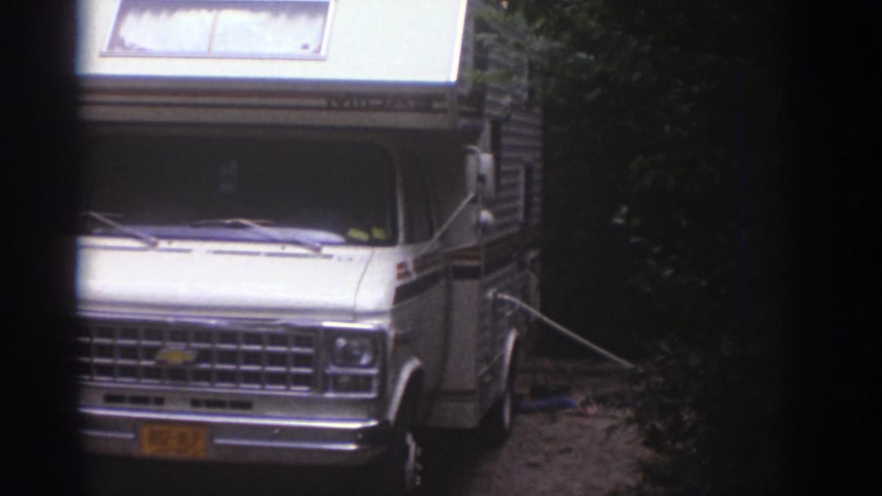 White Chevrolet-style motorhome with raised camper roof parked in a wooded Watkins Glen campsite in 1976 footage.