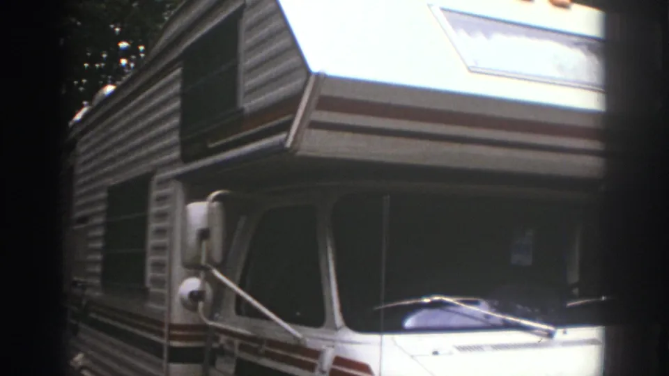 Home-movie view of the parked Watkins Glen motorhome, with windshield, wiper, side mirror, and striped bodywork visible.
