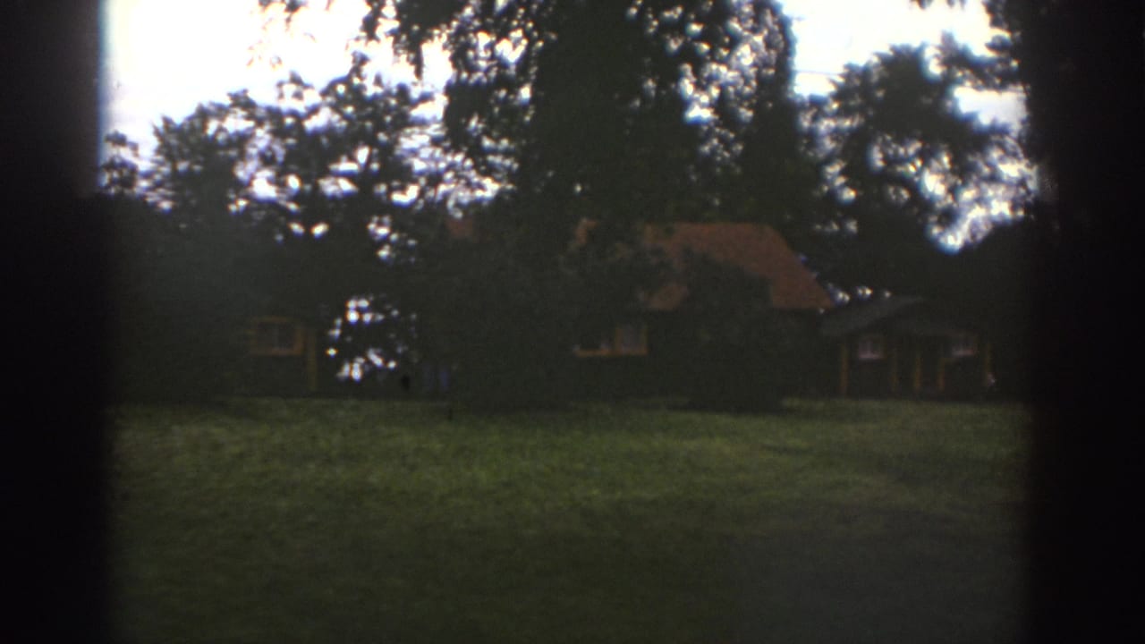 1976 Watkins Glen home-movie frame of a rustic cabin seen across a grassy wooded area.