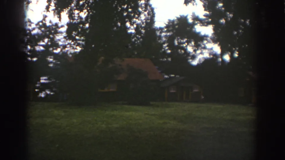 1976 Watkins Glen home-movie frame showing the cabin more centrally through dark tree shade.
