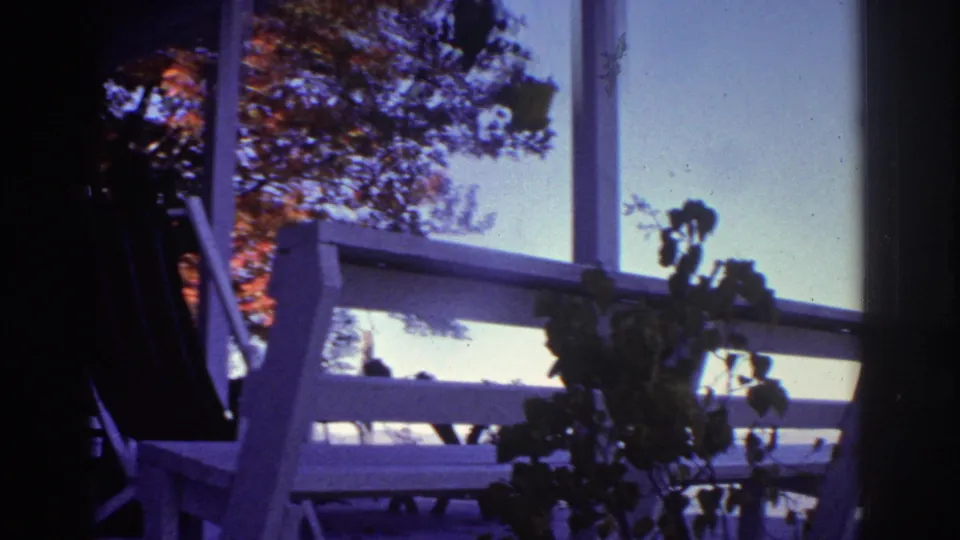 1976 8mm frame from Watkins Glen showing a white wooden overlook railing, foliage, tree shade, and pale sky.