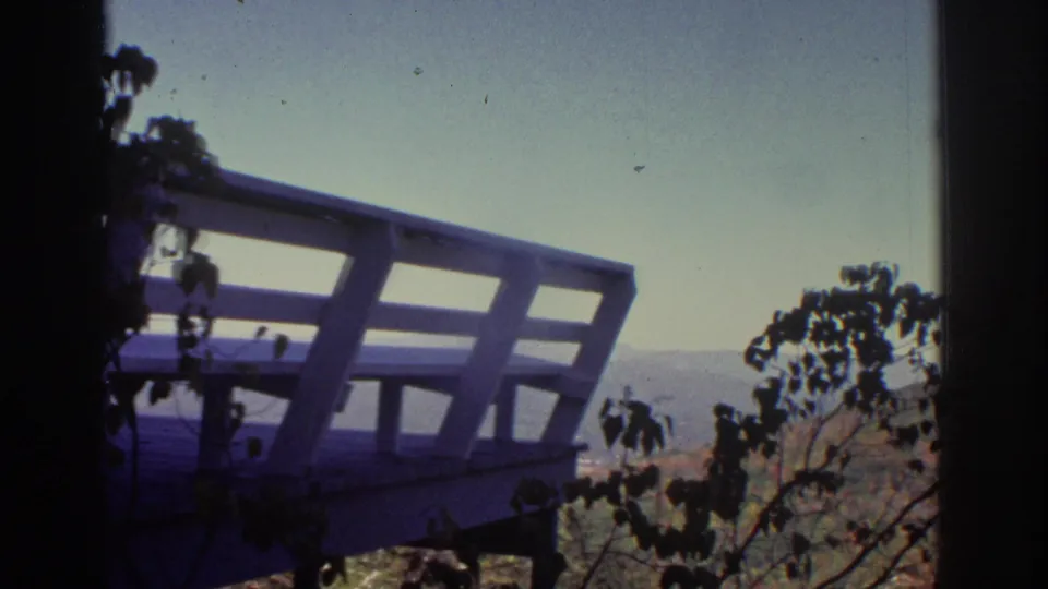 Handheld 8mm view from the elevated Watkins Glen overlook, with angled railing, foreground leaves, and a hazy valley distance.