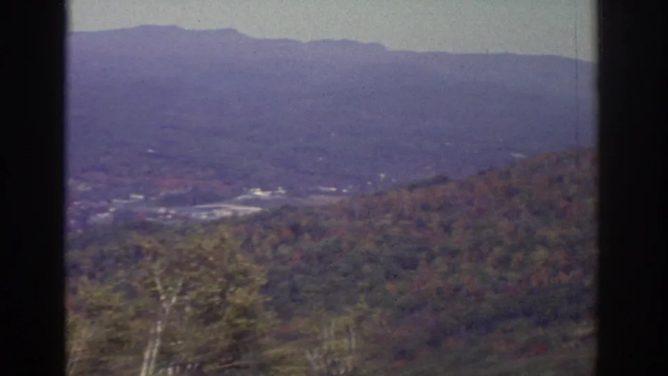 Watkins Glen-area landscape with autumn-toned forest, hazy ridge line, and a small light-toned developed area visible in the valley.