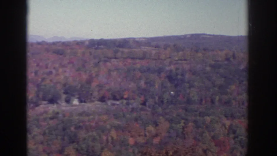 1976 8mm landscape near Watkins Glen with autumn trees, rolling hills, a distant ridge, and small pale structures in the valley.