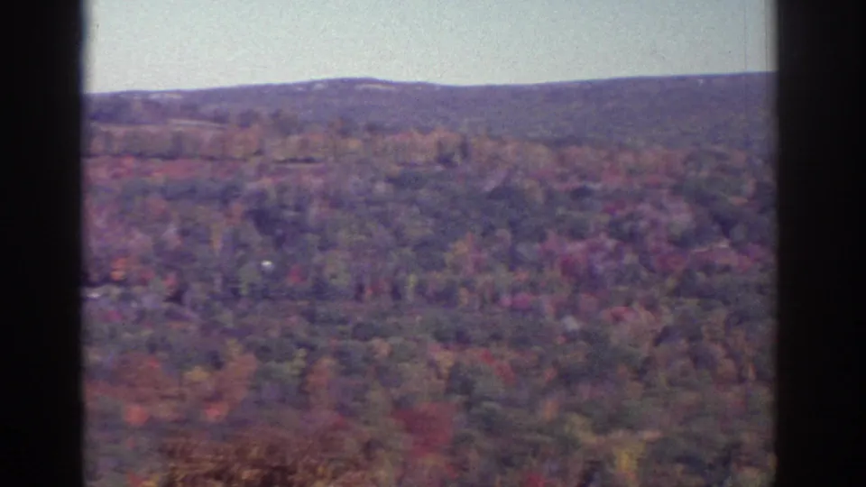 Watkins Glen-area 8mm frame of rolling autumn woods, hazy distant hills, pale sky, and visible film-gate edges.