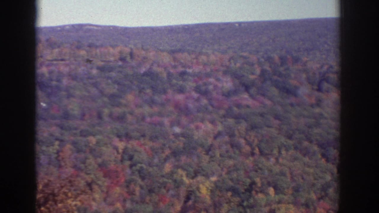 1976 8mm aerial footage near Watkins Glen showing wooded hills in autumn color beneath a soft horizon.