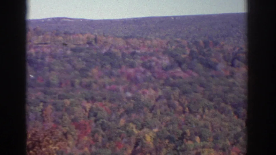 1976 8mm aerial footage near Watkins Glen showing wooded hills in autumn color beneath a soft horizon.