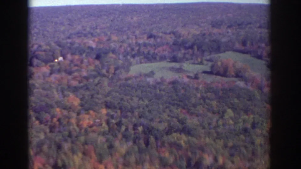 1976 aerial home-movie view near Watkins Glen with forested hills, open fields, and soft 8mm color.