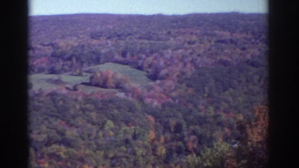 Watkins Glen-area aerial frame from 1976 showing autumn woods, fields, and distant hills on 8mm film.