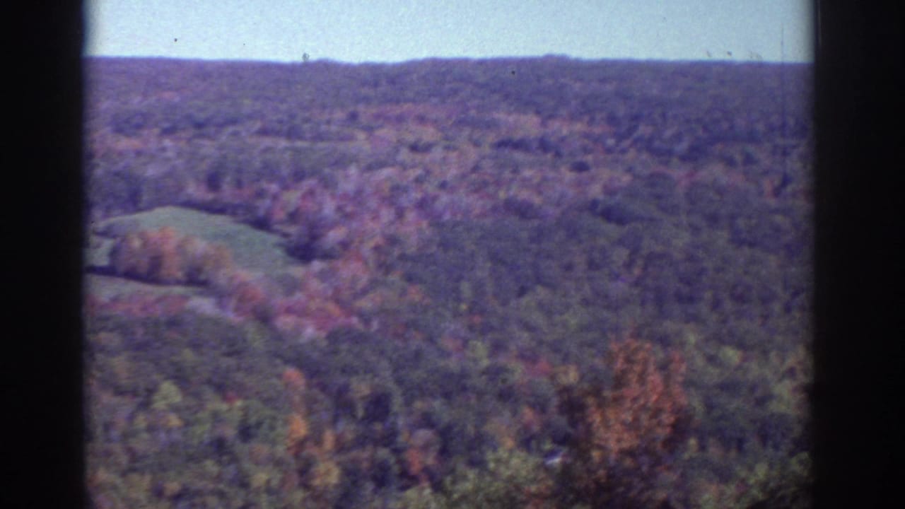 1976 Watkins Glen-area 8mm view of wooded hills covered in fall foliage, framed by dark vertical borders and a pale sky.