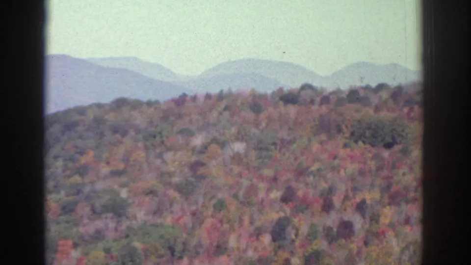 1976 8mm landscape frame showing colorful autumn treetops with distant blue hills near Watkins Glen, New York.