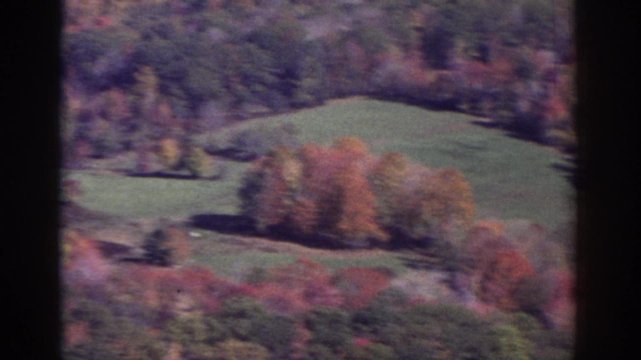 1976 Watkins Glen area valley view with green pasture, fall-colored trees, and dark window framing in a soft 8mm frame.