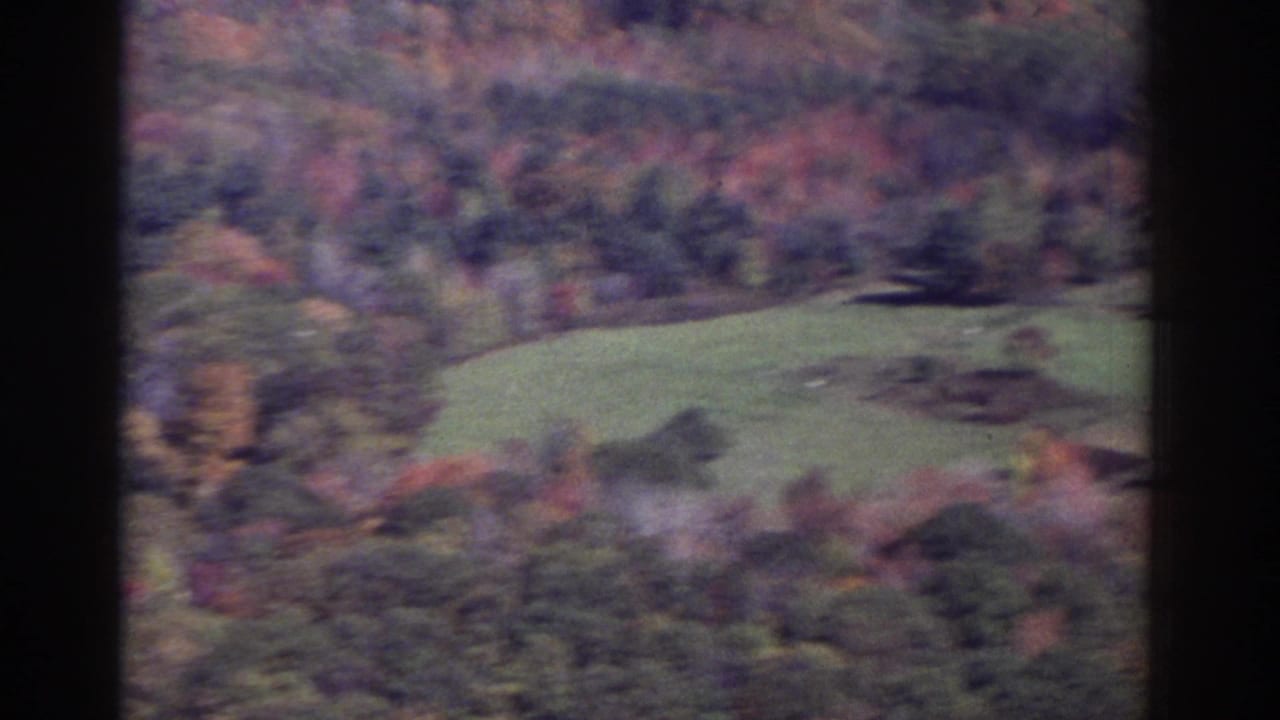 Wooded hills and patches of green field with autumn foliage, framed by dark vertical edges.