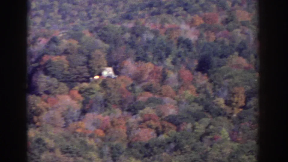 Soft 8mm view of a wooded Watkins Glen area valley in fall, including a small distant light-colored structure among the trees.