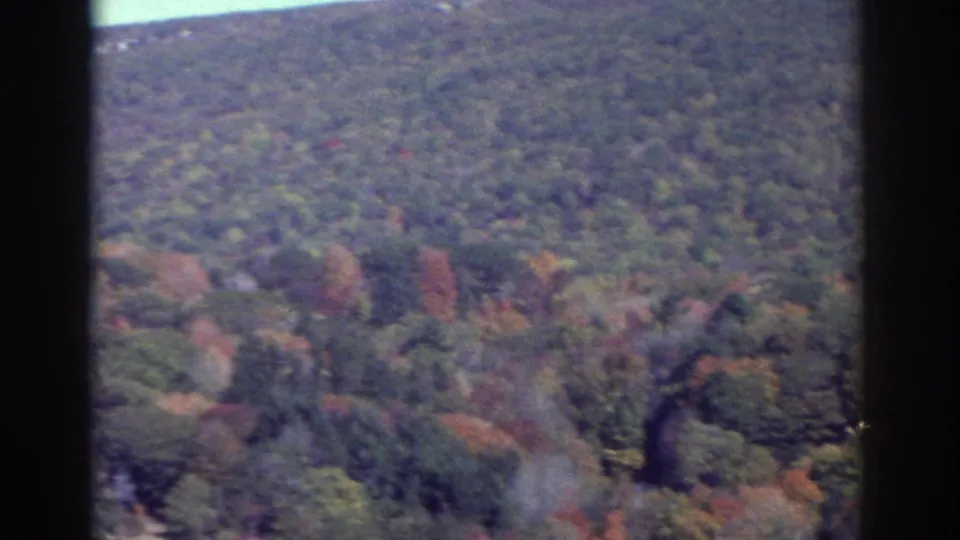 Elevated 1976 Watkins Glen area view of a wooded hillside with muted autumn color, dark window framing, and visible 8mm grain.
