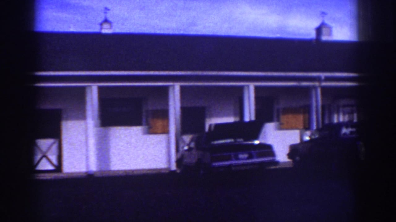 1976 Watkins Glen home-movie frame showing a white motel-style exterior, porch columns, and parked cars under a dark roof.