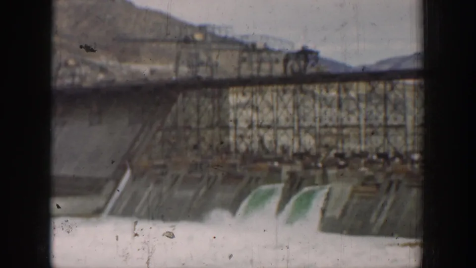 Large California dam works with spillway water and a steel trestle structure, seen in soft 8mm color.