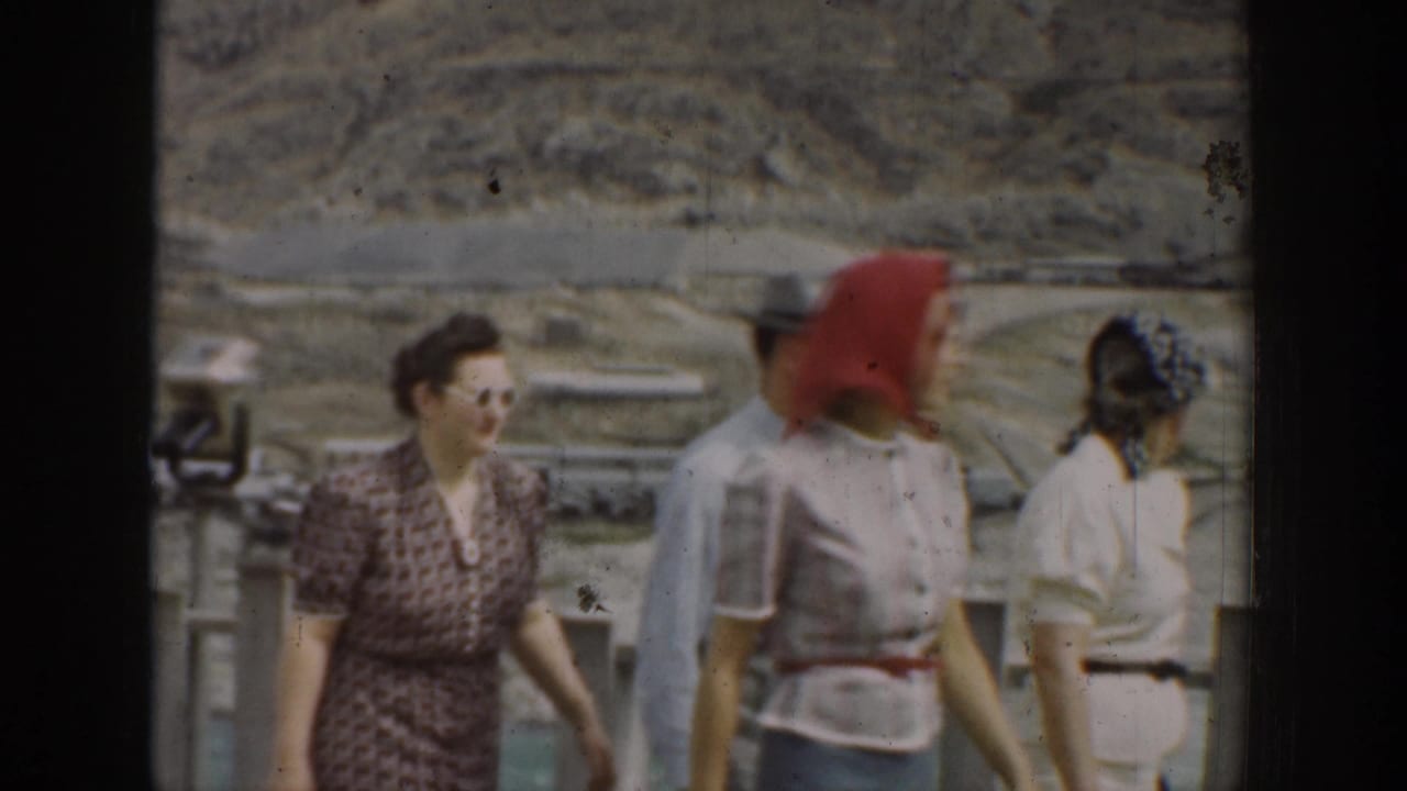 Group of adults walking past a fence, including a woman in a red headscarf.