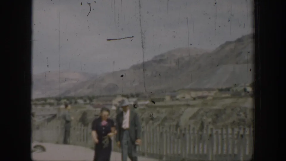 1937 California rural frame with two adults near a fence, set against dry hills and muted 8mm color.