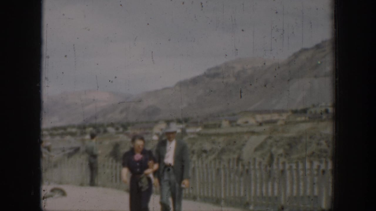 Adult couple walking along a dam overlook with a fence and arid hills behind them.