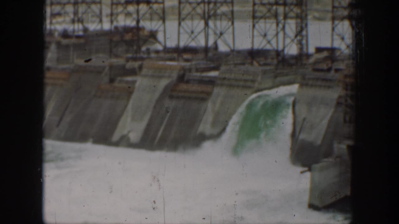 1937 California home-movie view of a concrete dam spillway with water pouring over one section and metal work above.