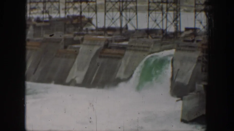 1937 California home-movie view of a concrete dam spillway with water pouring over one section and metal work above.