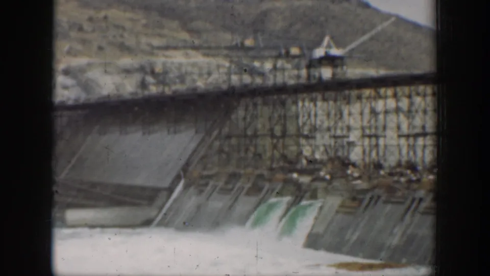 1937 California 8mm frame showing the dam spillway, railing, hillside, and water through heavy frame borders.