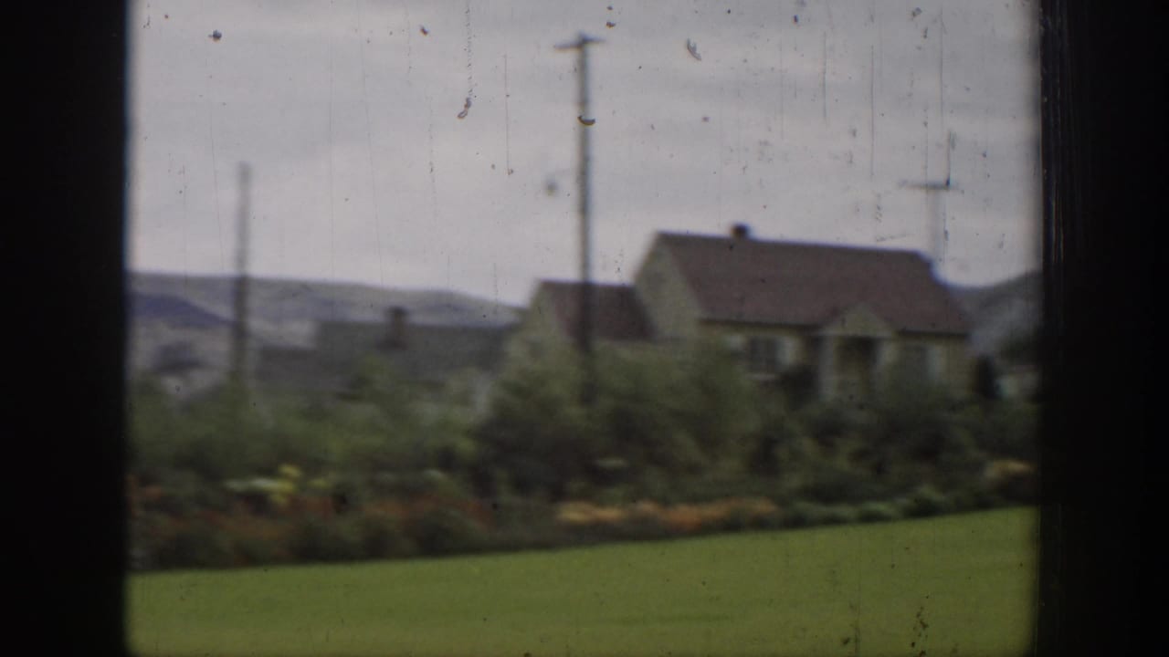 Rural house and green yard seen through dark window or film-frame edges.
