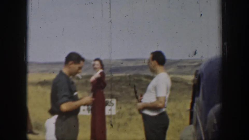 1937 California home-movie frame showing adults gathered beside cars in a dry open landscape with low hills beyond.