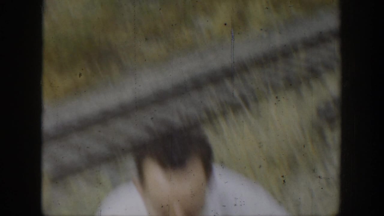 Blurred person near a dark vertical frame with dry ground and hillside beyond.