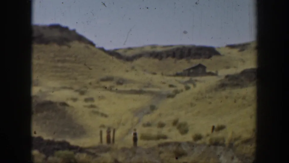 1937 California 8mm frame showing dry rolling terrain, a small distant structure, and a lone figure in the landscape.