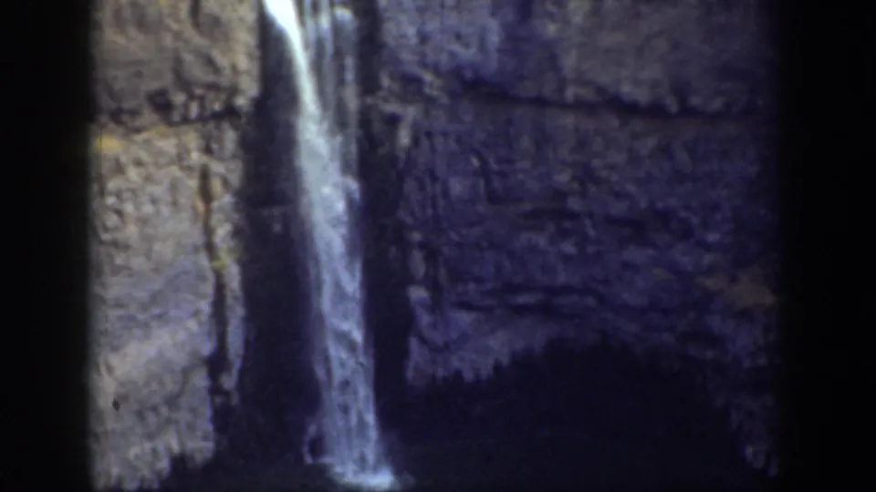 1937 California 8mm frame of a waterfall descending along layered rock into a shadowed lower area.