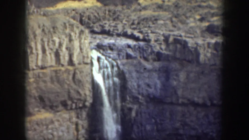 Vintage 8mm California frame showing a waterfall spilling over stratified rock in an arid canyon landscape.