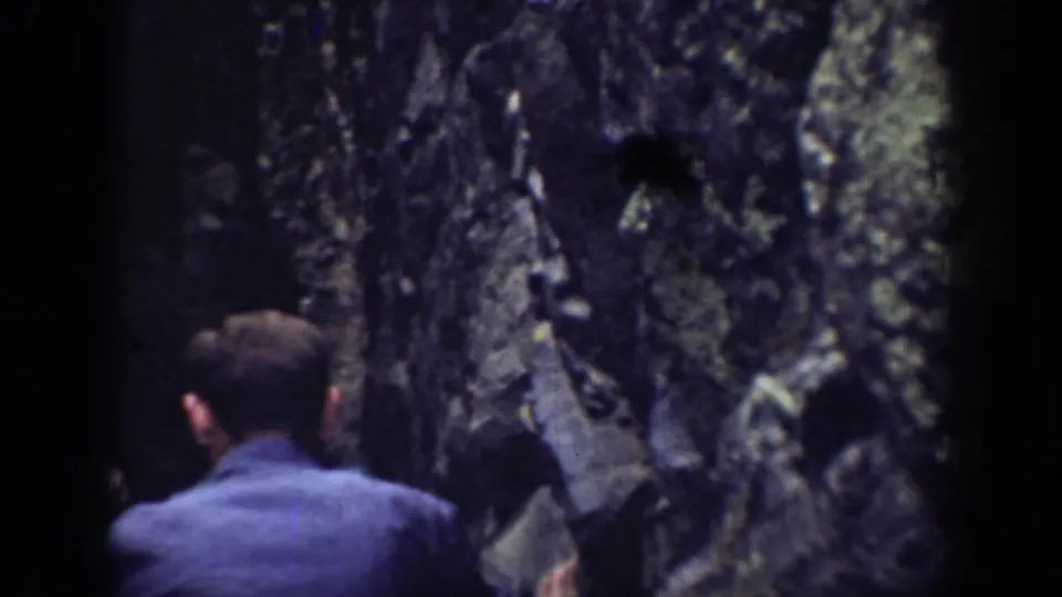 Handheld frame from the California outing showing a person from behind near shadowed jagged rock formations.