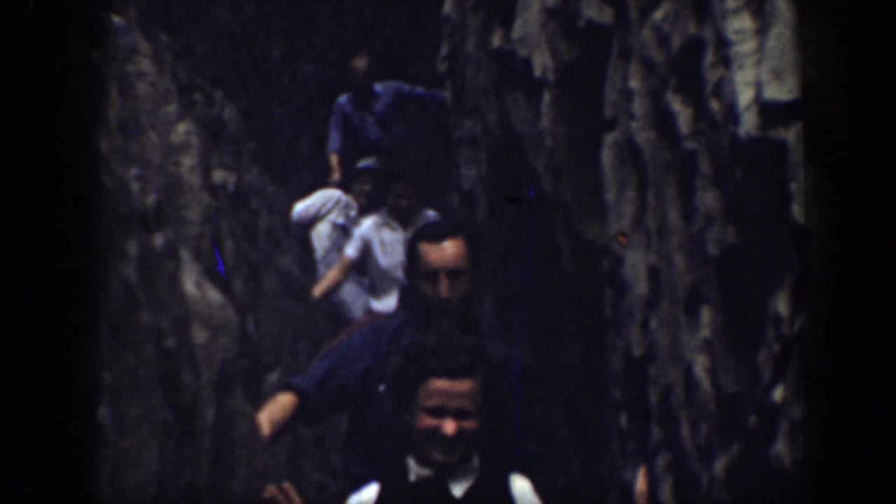 1937 California home-movie frame of people in a narrow stone passage, including a man in a white shirt and dark vest looking toward camera.