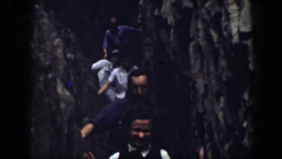 1937 California home-movie frame of people in a narrow stone passage, including a man in a white shirt and dark vest looking toward camera.