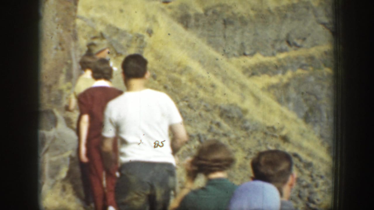 1937 California frame showing a small group walking along a rocky dam or slope, with dry terrain and handheld framing.