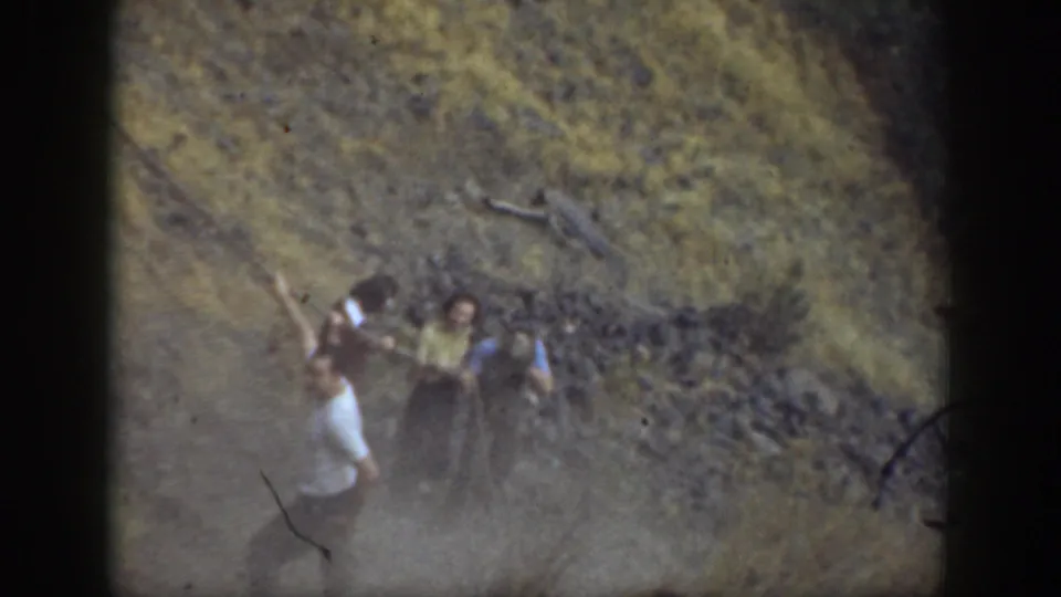 1937 California frame with several people gathered near a rope on a rocky slope, filmed through faded 8mm color stock.