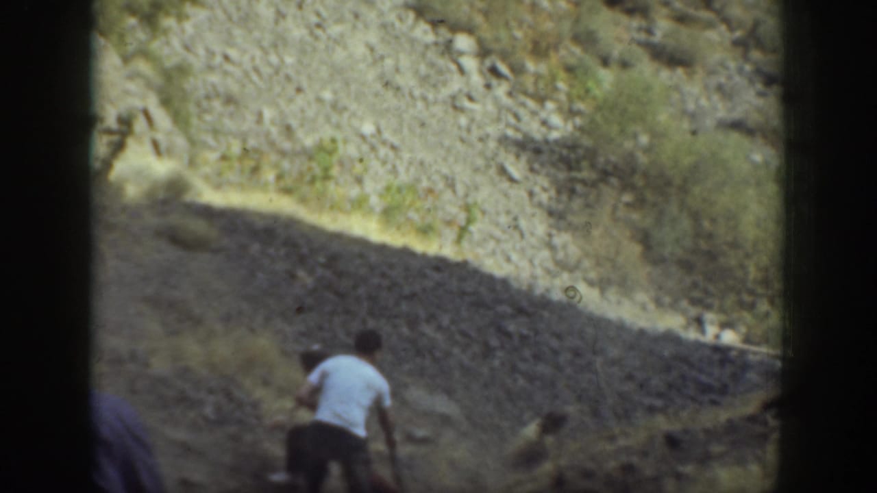 In 1937 California home-movie footage, adults appear to climb a steep rocky hillside in an arid landscape.
