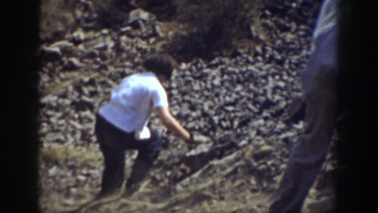 1937 California 8mm frame showing a person in a white shirt carefully moving over loose rocks on a hillside.