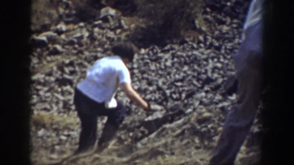 1937 California 8mm frame showing a person in a white shirt carefully moving over loose rocks on a hillside.