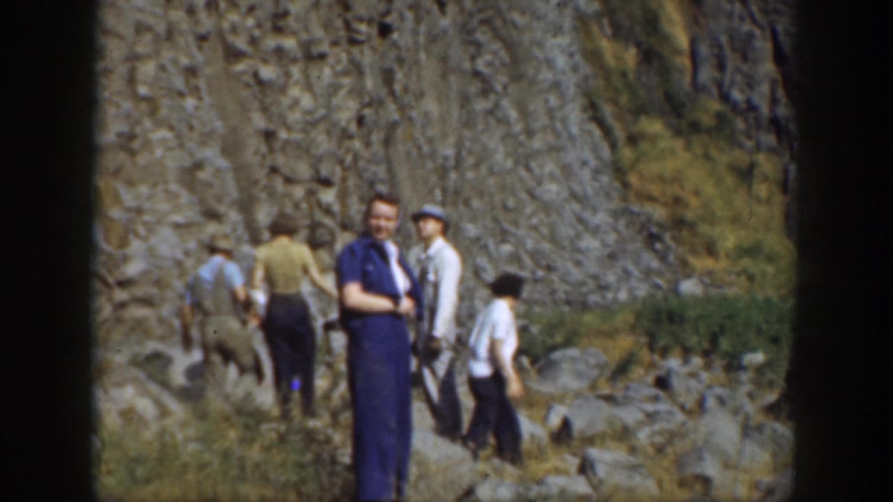 Group of tourists standing and walking among rocks near a cliff.