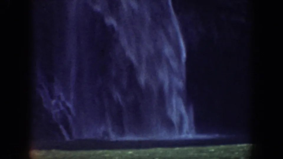 Dark cliff wall with a broad waterfall descending into a greenish pool or waterline in archival California footage.