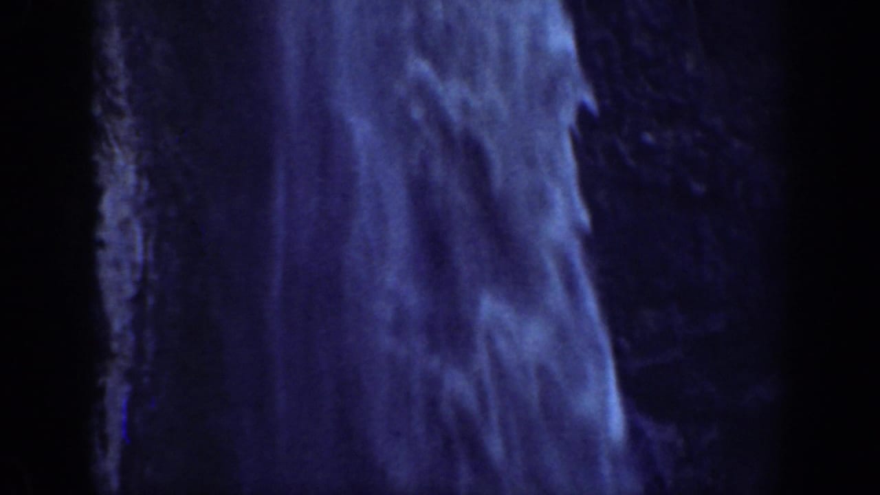1937 California 8mm frame showing a dark, blue-tinted close view of rushing waterfall beside rugged rock.