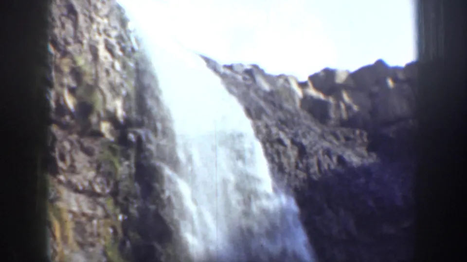 1937 California 8mm frame with a waterfall pouring down sunlit rocky cliffs beneath bright sky.