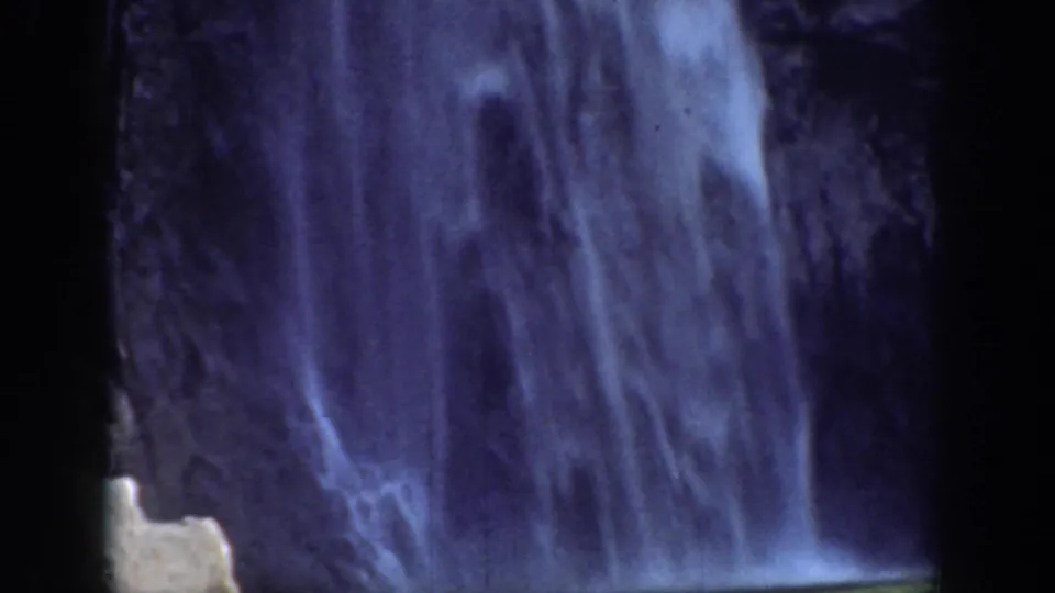 1937 California 8mm frame showing the waterfall descending along a dark rock wall with pale rocks near the base.